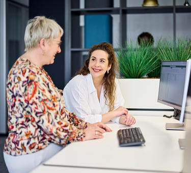 Two women standing at a desk looking at each other