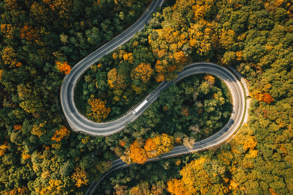 essentials-mobility-left.jpg Ein Elektrofahrzeug fährt auf einer kurvigen Straße durch herbstliche Bäume