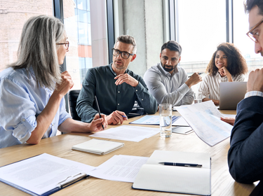 Personen, die an einem großen Tisch in einem Büro sitzen Personen, die an einem großen Tisch in einem Büro sitzen